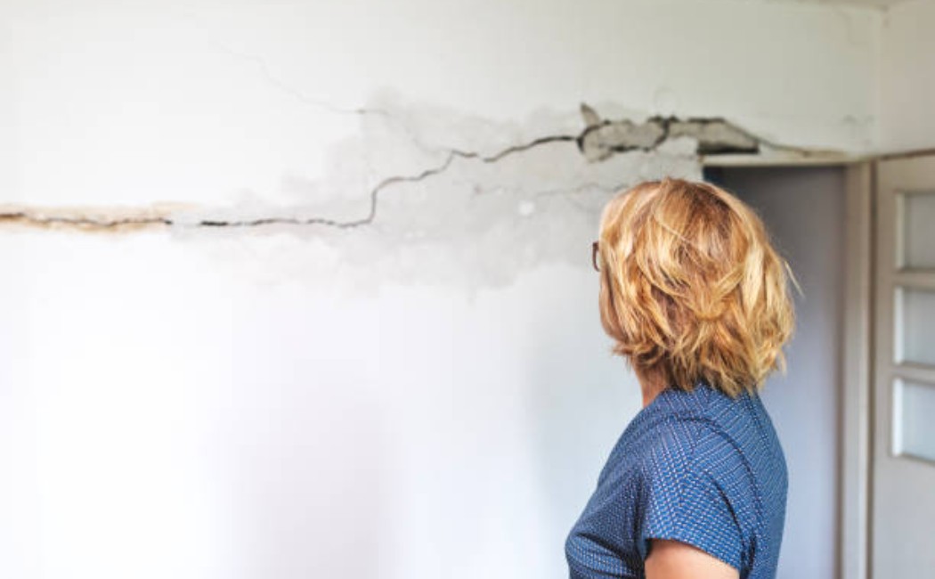 Woman inspecting earthquake-cracked plaster and broken wall.