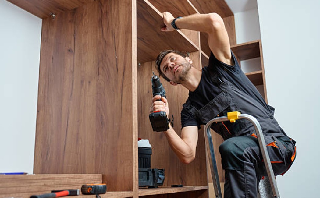 Man installing a wooden wardrobe with an electric drill