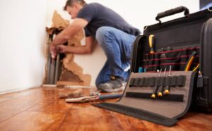 Plumber repairing a leaking pipe beneath a kitchen sink, water spraying while he works.