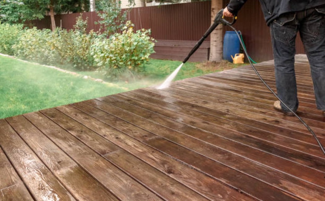 Person power‑washing outdoor wooden deck and wall surfaces.