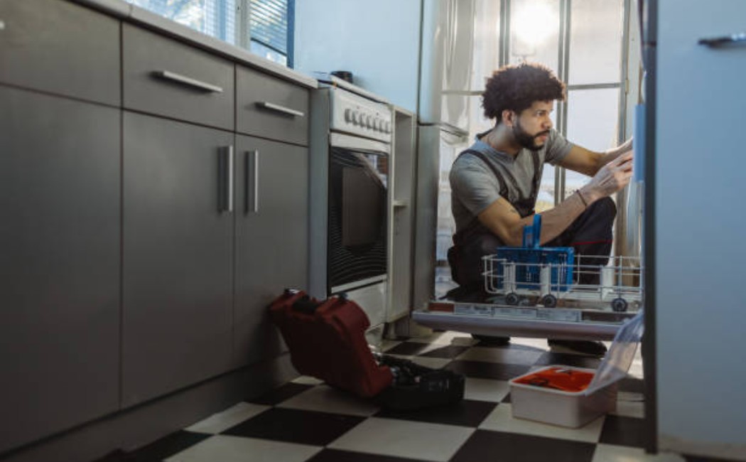 Home appliance service: man repairing dishwasher with focus.