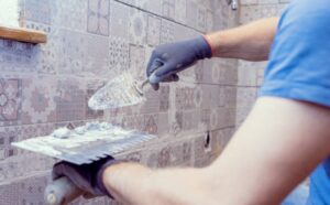 Man grouting kitchen wall tiles with a trowel.