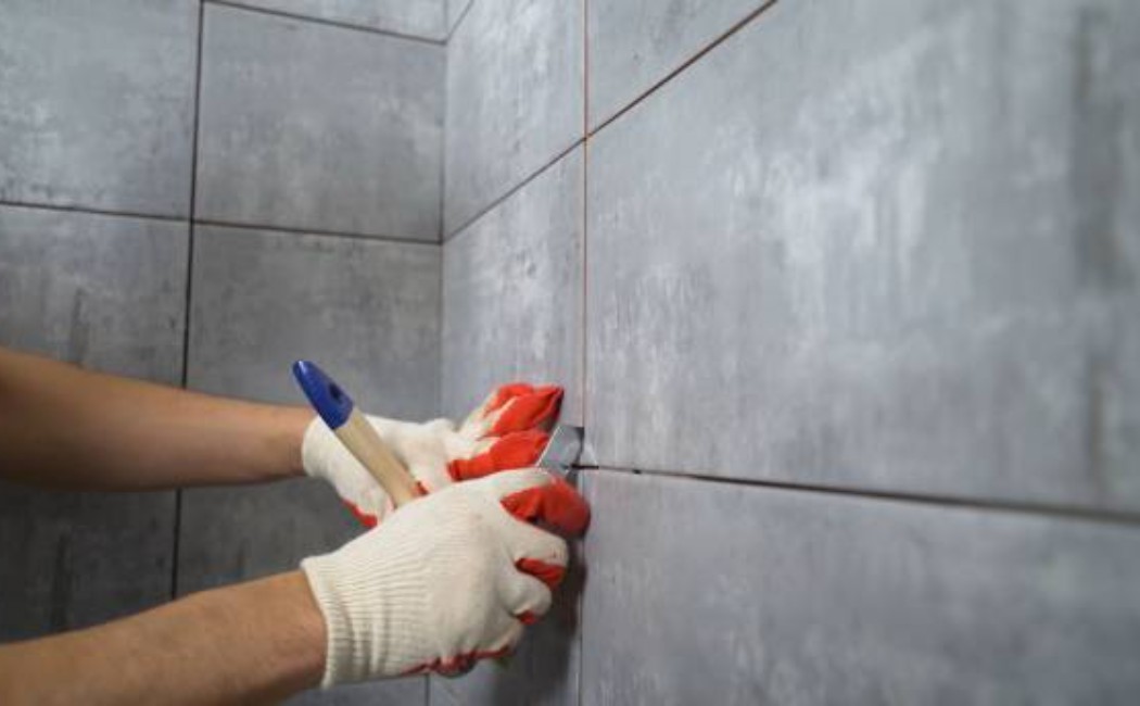 Worker applying grout between ceramic wall tiles.