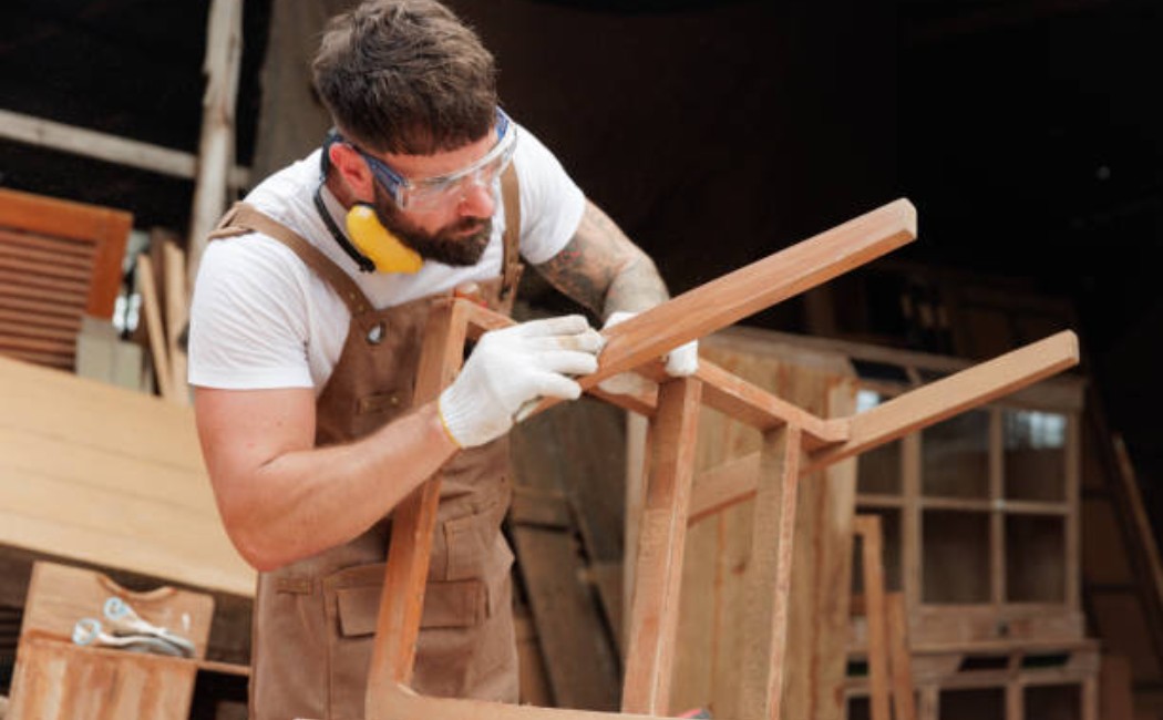 Furniture maker cleaning scrap wood from the wooden chair frame.