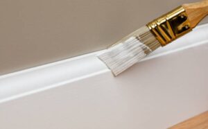 person painting white baseboard trim with a brush during home improvement project.