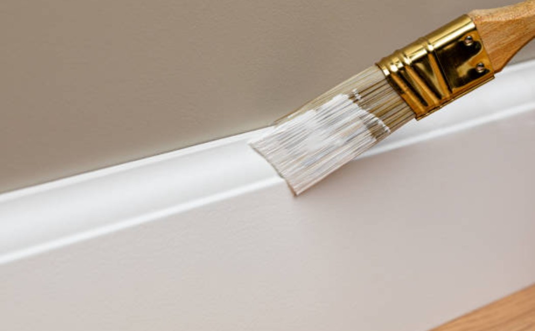 istockphoto-2181819567-612x612_1050x650_q90 person painting white baseboard trim with a brush during home improvement project.