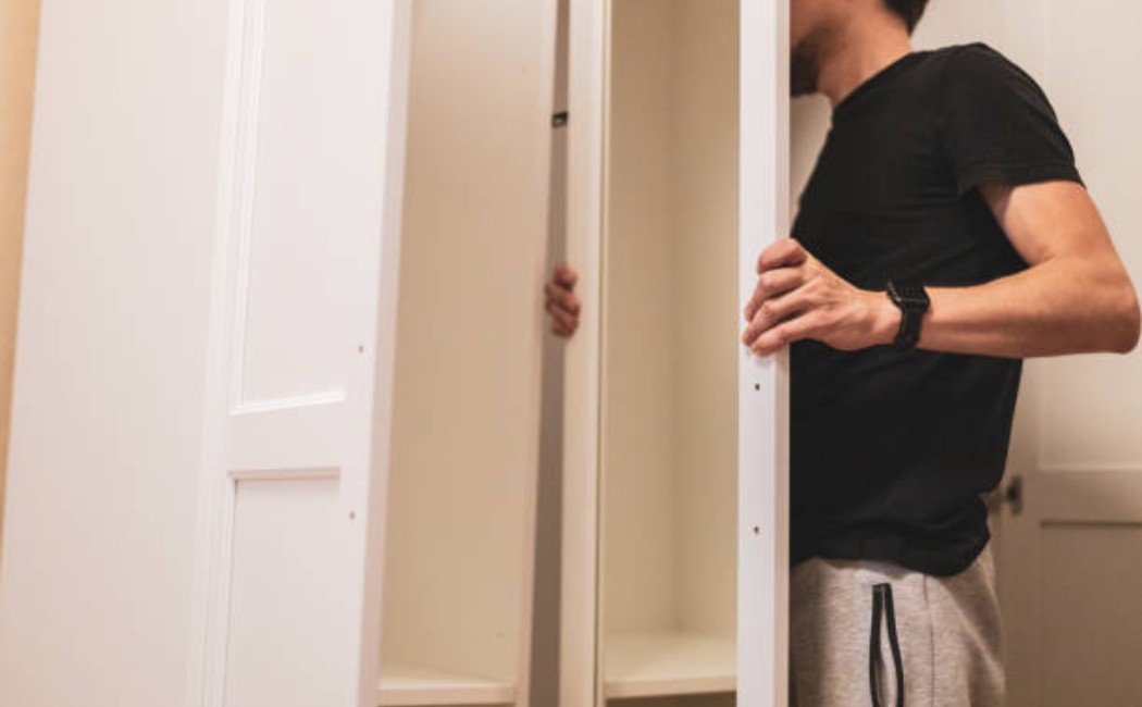 A young man is opening the mirrored wardrobe door at home