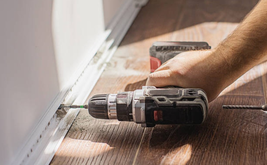 Person installing baseboards and drilling into a wall.