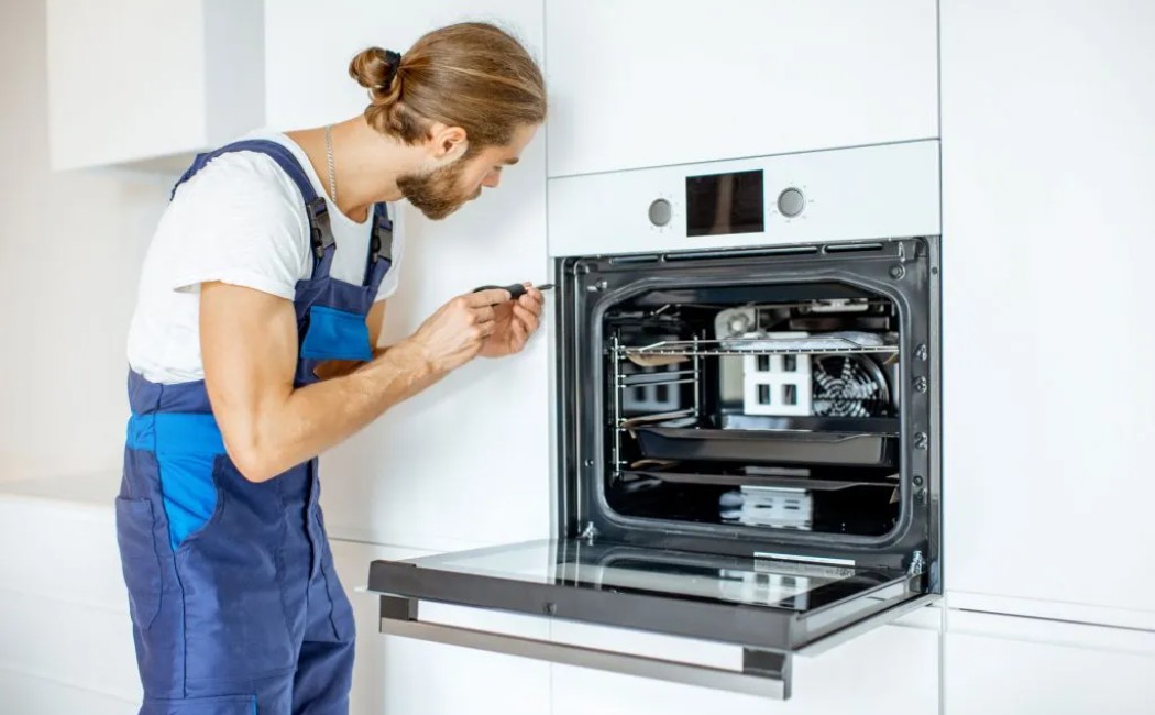 Technician performing Appliance Repair Services while inspecting an open built-in oven in a modern kitchen.