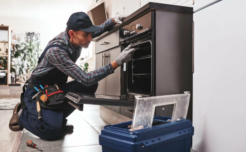 Technician performing Appliance Repair Services while fixing a built-in kitchen oven using tools in a modern home kitchen.