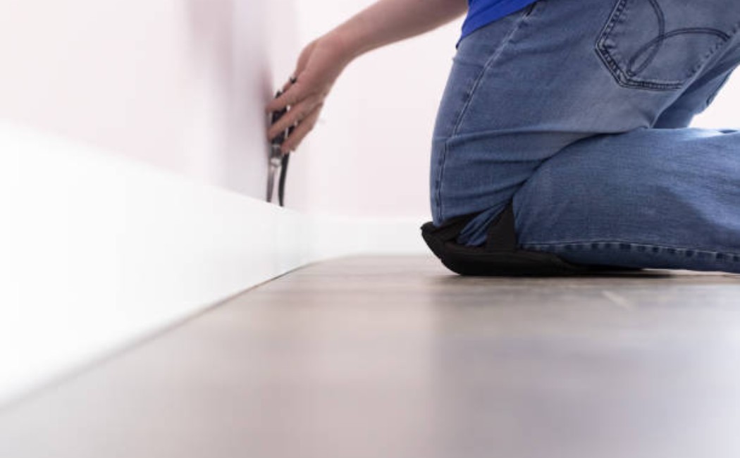 Baseboards and Molding Services: Installing Wall Trim Indoors Person kneeling on floor installing trim along wall, showcasing Baseboards and Molding Services in a home interior setting.