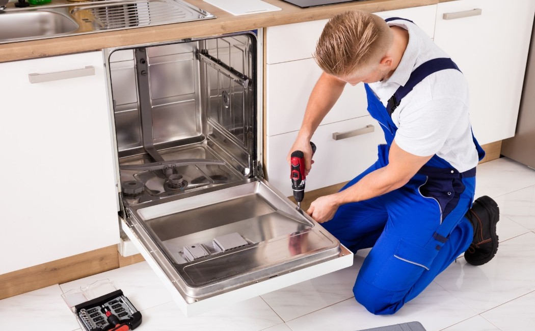 Repair specialist providing Appliance Repair Services while fixing an open dishwasher in a modern kitchen.