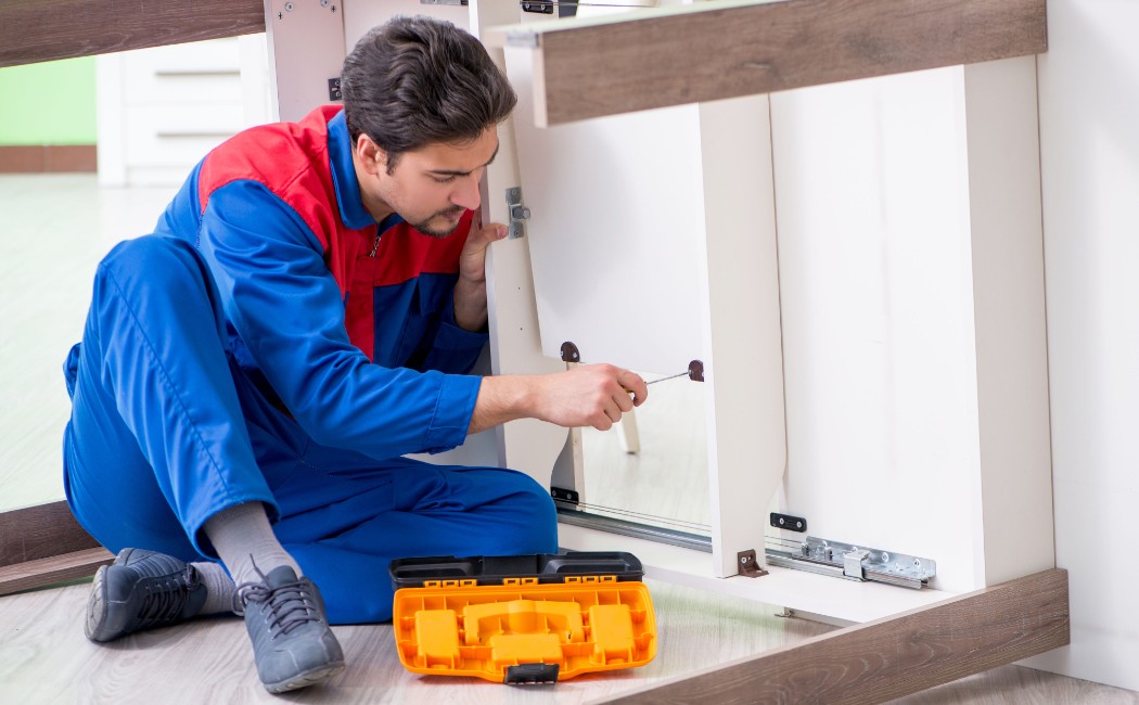 Technician providing Furniture Repair Services while fixing a wooden cabinet with tools on the floor.