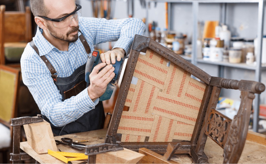 Technician providing Furniture Repair Services while restoring a wooden chair in a workshop using power tools.