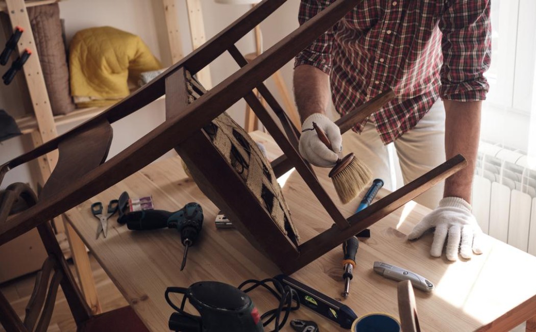 Craftsman performing Furniture Repair Services by refinishing and restoring a wooden chair in a workshop.