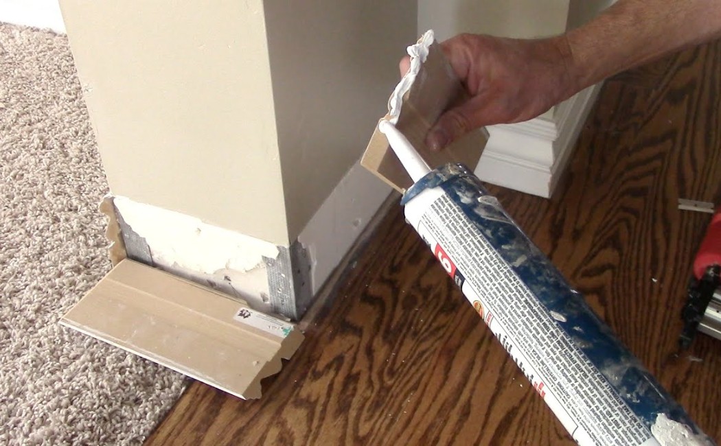 Trim Molding Installation and Baseboard Repair. Handyman applying adhesive and installing trim molding during Baseboard Repair Services on an interior wall corner.