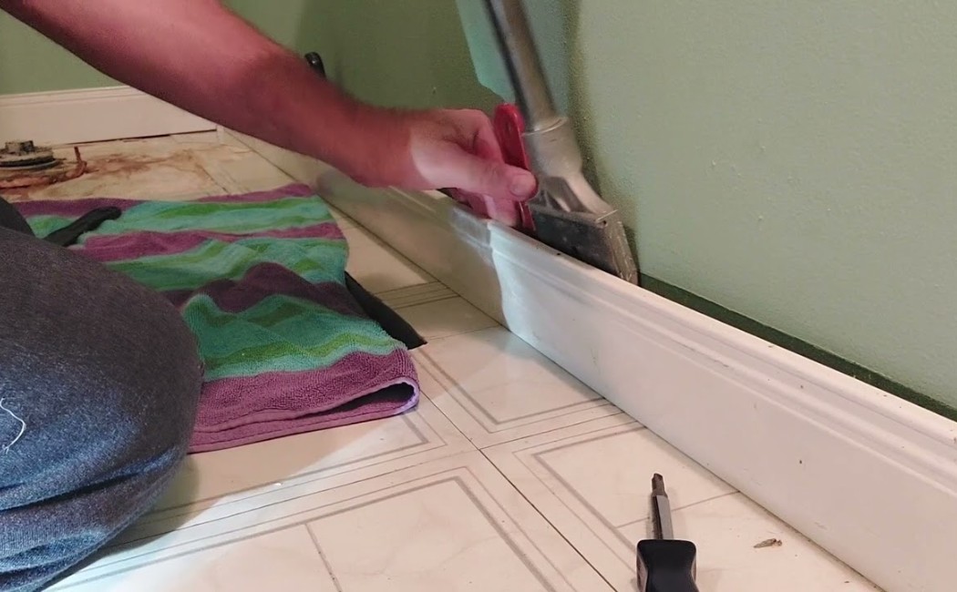 Baseboard Repair Near Tiled Flooring. Worker removing and repairing wall trim near tiled flooring during professional Baseboard Repair Services in a home interior.
