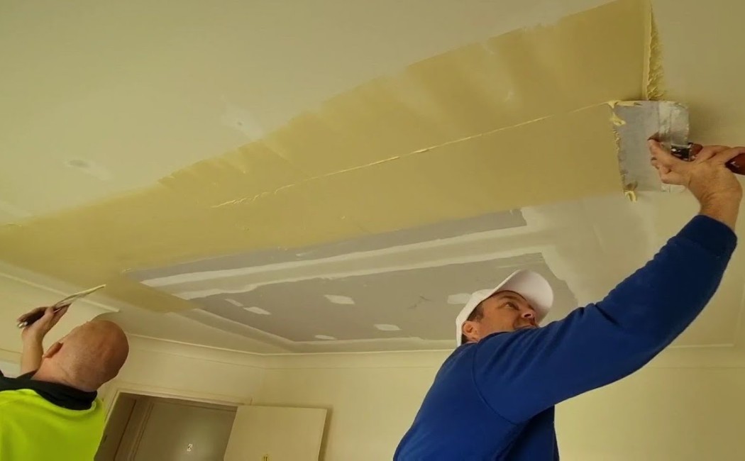 Technicians smoothing joint compound on a ceiling during Drywall Repair Services in a residential interior.