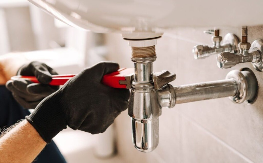 Experienced plumbing company technician repairing a bathroom sink drain pipe using professional plumbing tools.