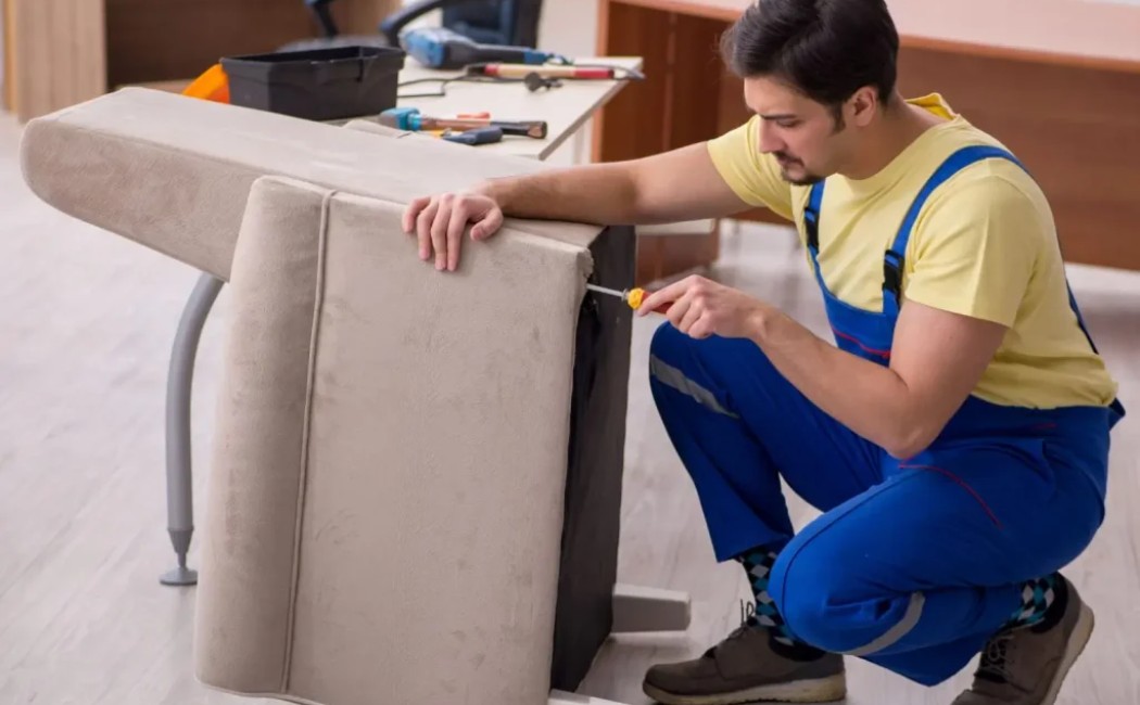 Furniture repair expert fixing an upholstered chair with hand tools during an indoor furniture restoration project.