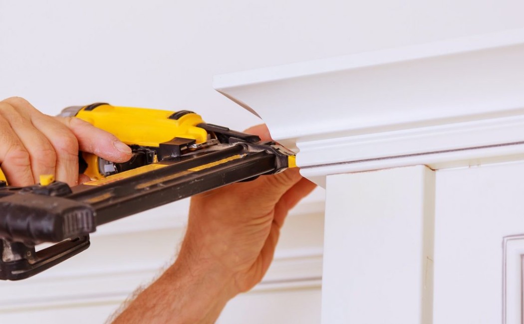Crown molding installation expert securing crown molding with a nail gun for a seamless interior trim installation.
