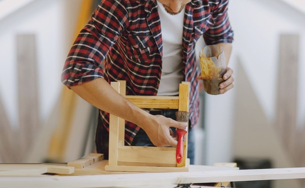 Furniture Repair Wood Staining Service. Furniture repair professional applying wood stain to a handcrafted wooden chair in a woodworking workshop.