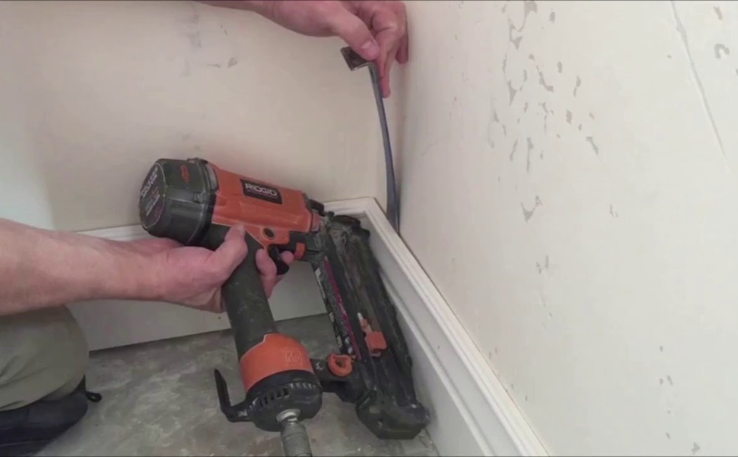 Molding Repair Specialist Fixing Baseboard Trim. A molding repair specialist securing baseboard molding with a finish nailer for a seamless wall trim restoration.